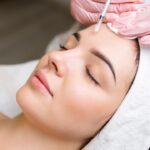Close up of hands of cosmetologist injecting botox in female face