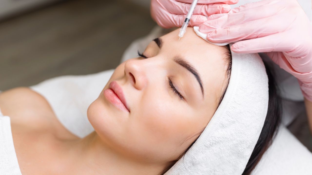 Close up of hands of cosmetologist injecting botox in female face